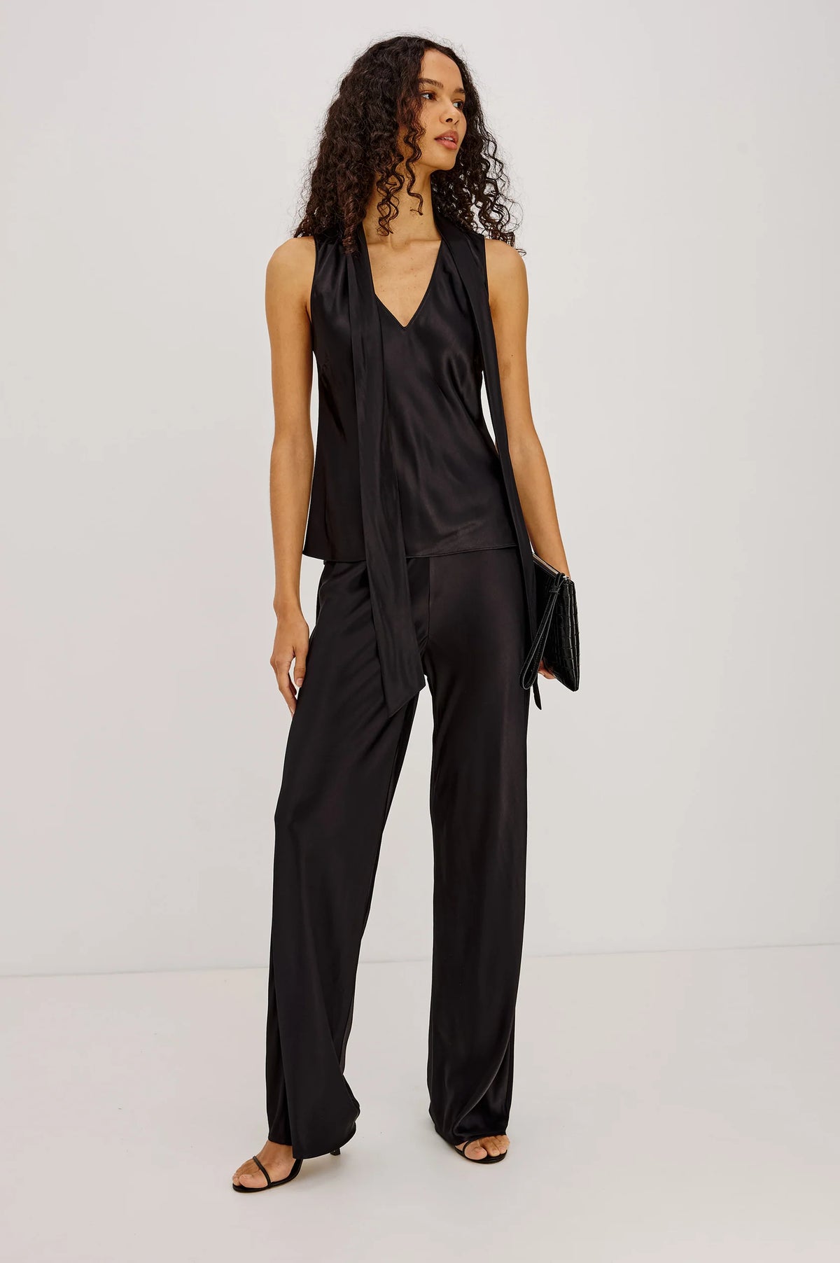 Woman wearing a black satin top and black pants against a plain background
