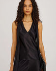 Woman wearing a black sleeveless top and pants with a clutch against a light gray background
