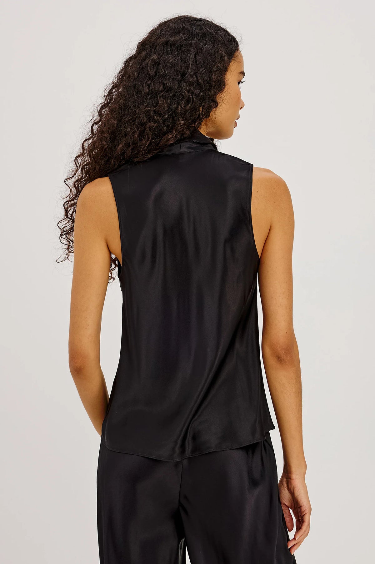 Woman wearing a black sleeveless top and pants on a plain background