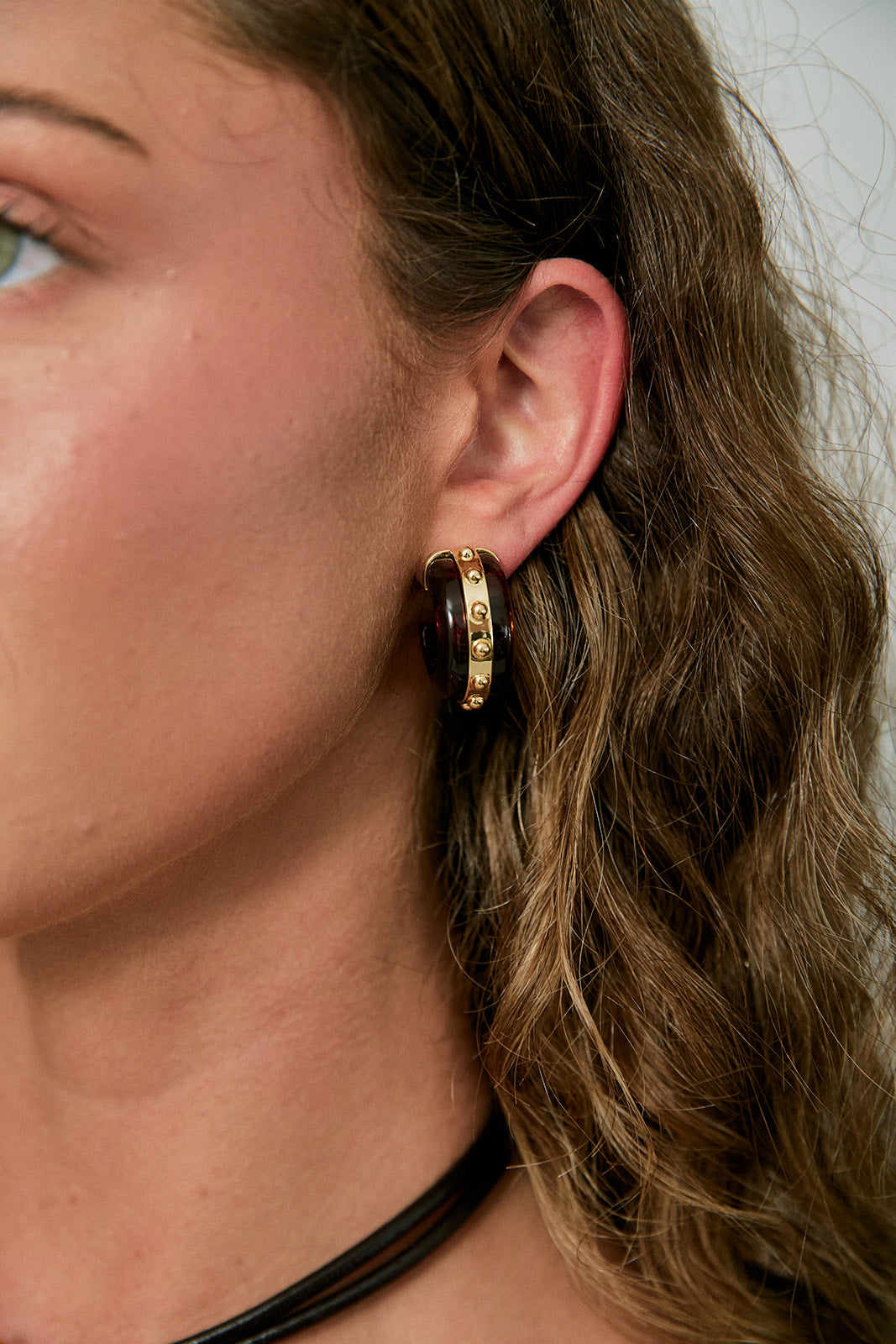 Close-up of a person wearing a gold hoop earring with a neutral background