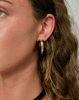 Close-up of a person wearing a gold hoop earring with a neutral background