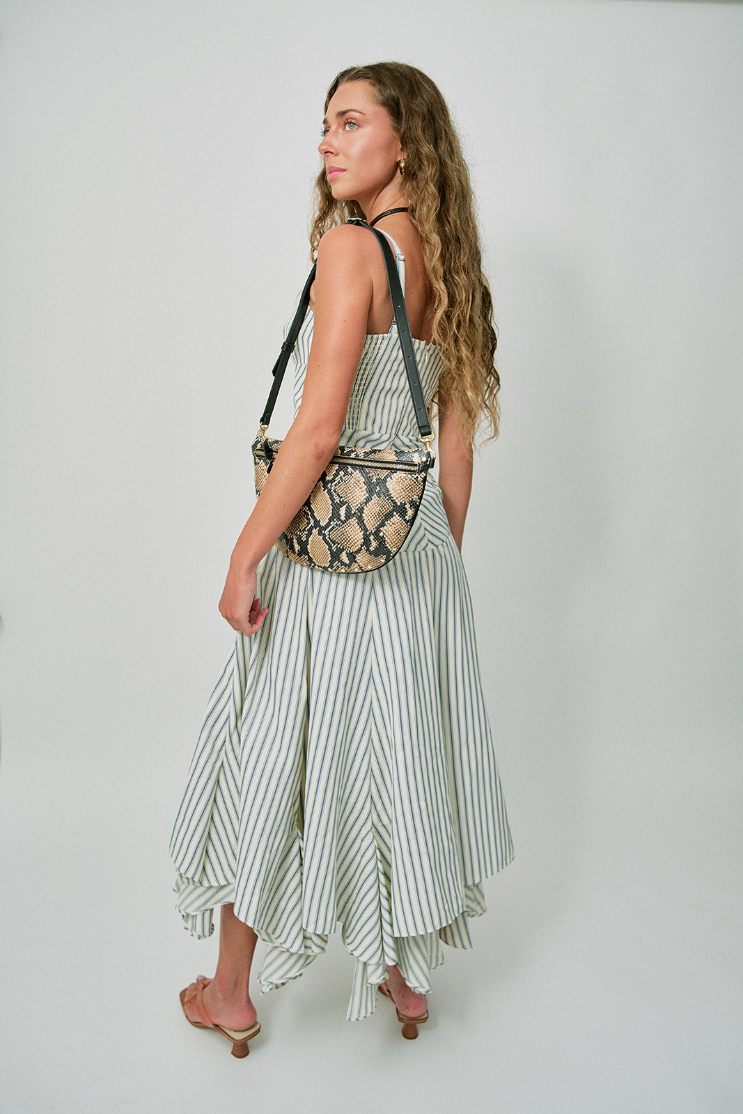 Woman wearing a striped dress with a patterned bag on a plain background back view with Brevel Vinyl Heels