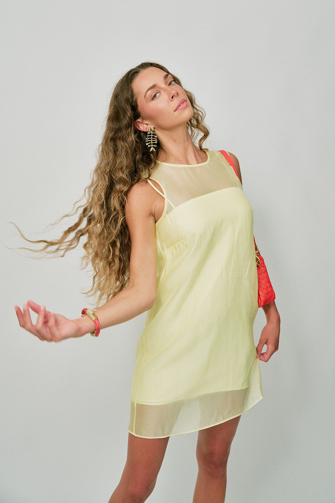 Woman wearing a light yellow dress with a red bag on a plain background with Josefina Earrings
