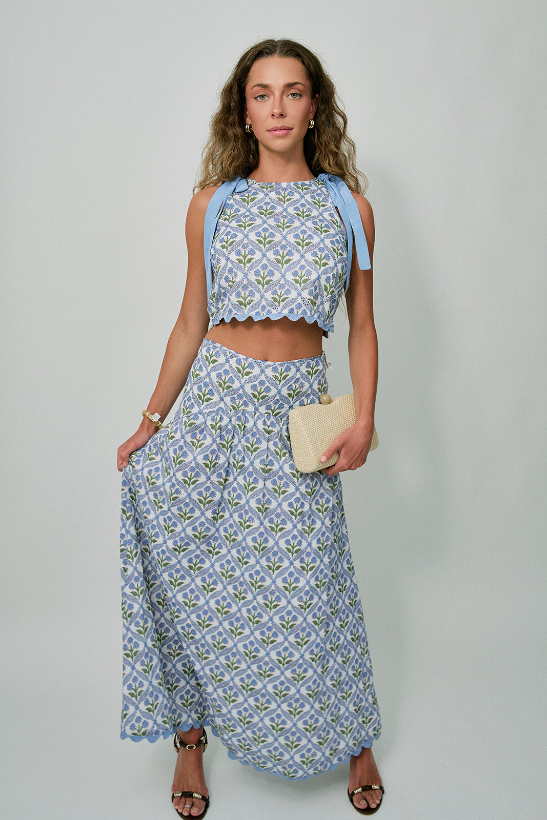 Woman wearing a blue floral outfit with tan clutch on a plain background