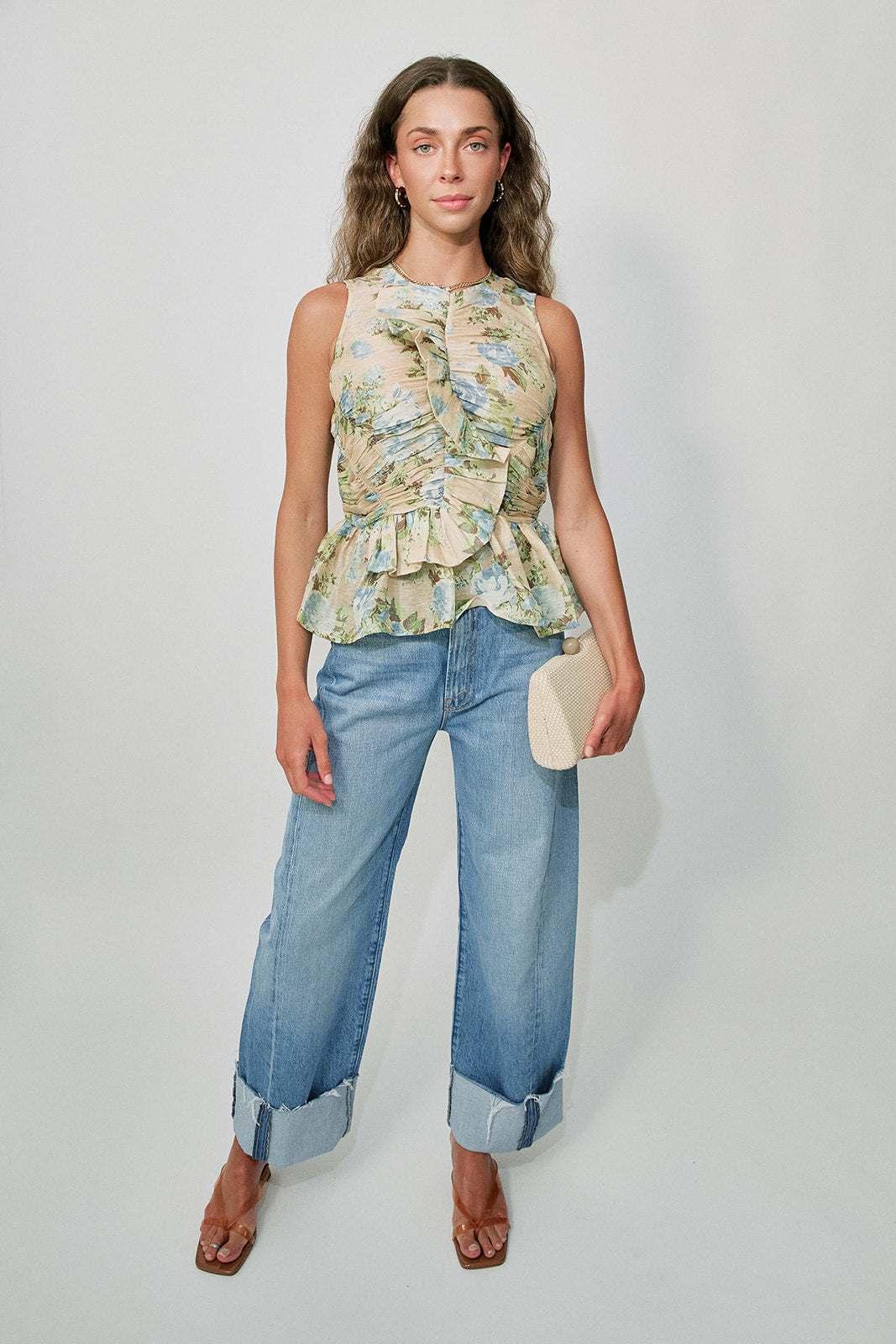 Woman wearing a floral sleeveless top and blue jeans against a plain background, full body front