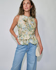 Woman wearing a floral sleeveless top and blue jeans against a plain background