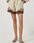 Person wearing a cream outfit with embroidered shorts on a white background