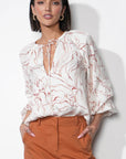 Woman wearing a white blouse with red patterns and orange pants against a white background