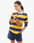 A woman modeling a yellow and navy blue horizontally striped long-sleeve polo shirt with a white collar, paired with navy shorts and a brown suede crossbody bag, against a plain white background.