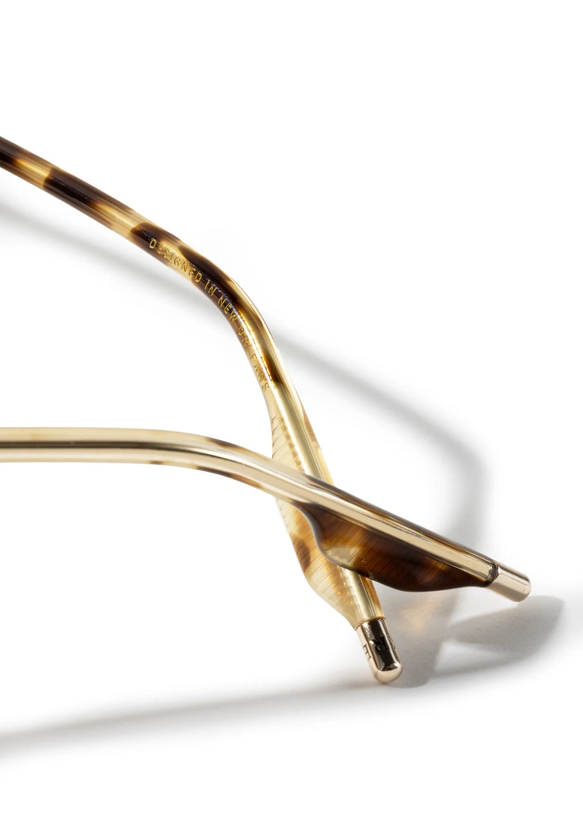 Close-up of a pair of designer sunglasses showing the gold metal temples and tortoiseshell acetate arms, set against a clean white background with a soft shadow.