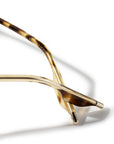 Close-up of a pair of designer sunglasses showing the gold metal temples and tortoiseshell acetate arms, set against a clean white background with a soft shadow.