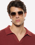 A man wearing round gold-framed sunglasses with brown lenses and a textured burgundy polo shirt, photographed against a clean white background.