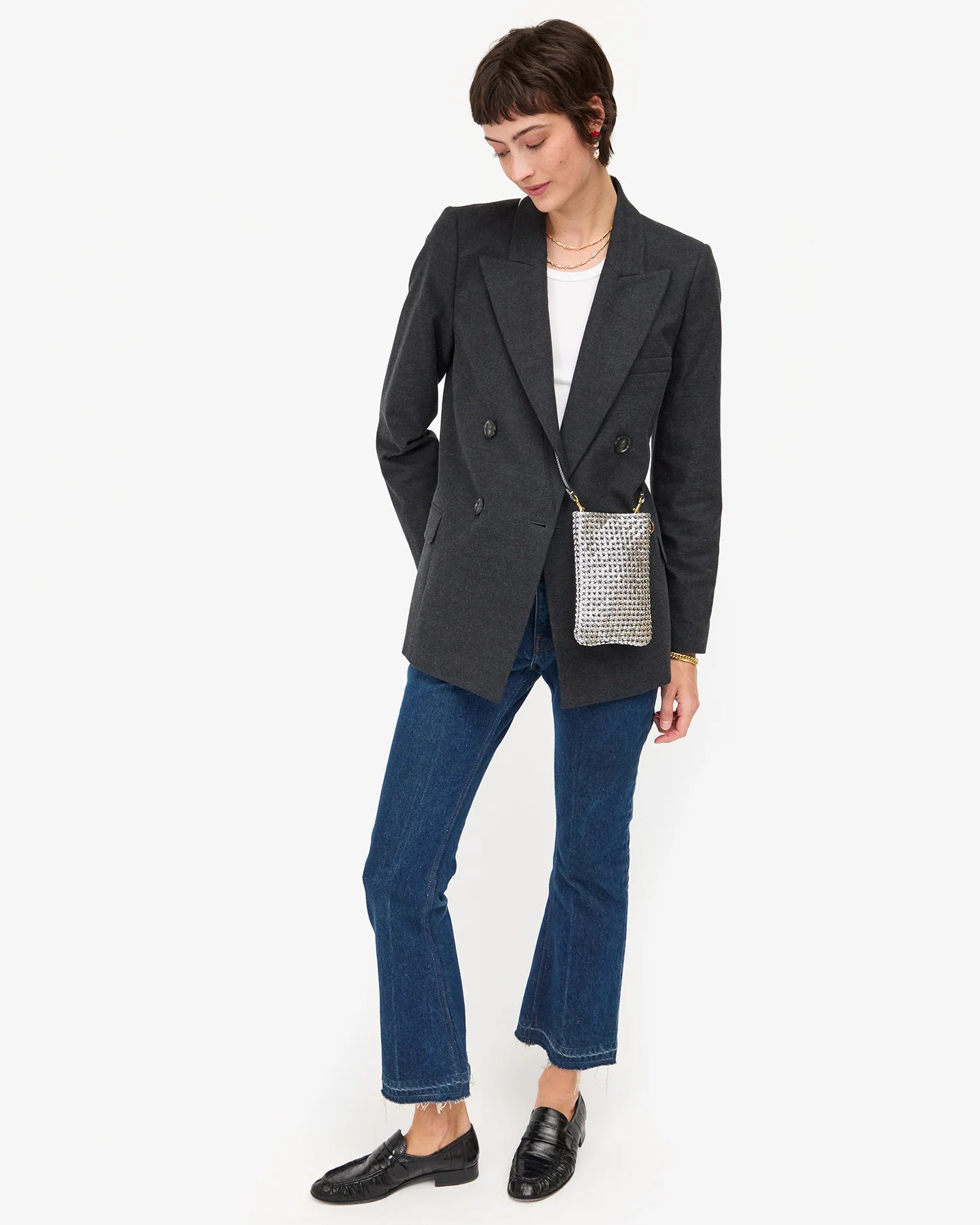 Woman wearing a dark gray blazer, blue jeans, and black shoes on a white background