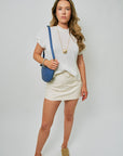 Woman wearing a white t-shirt and beige skirt with a blue bag on a plain background