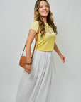 Woman wearing a yellow t-shirt and white skirt with a brown bag on a plain background, side view