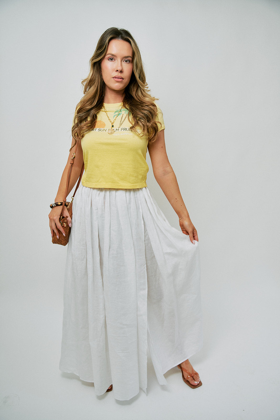 Woman wearing a yellow top and white skirt on a plain background, full body front