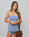 Woman wearing a blue and white striped strapless set with a brown handbag and Shell Choker on a gray background