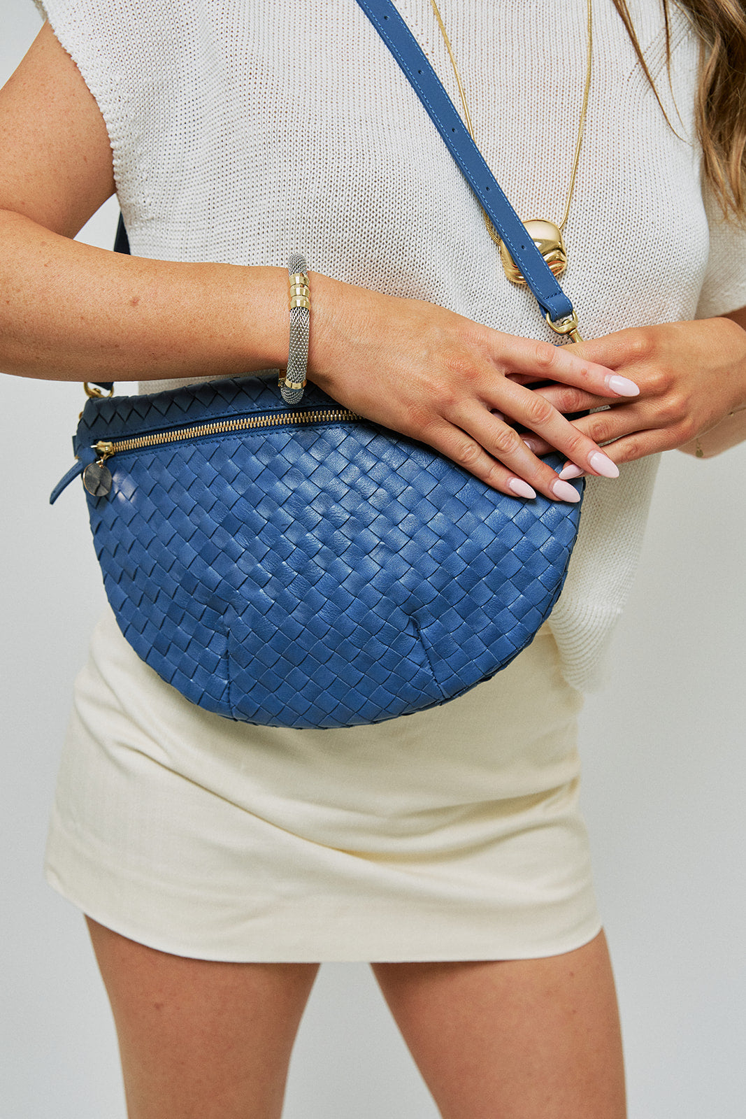 Person wearing a blue woven handbag on a plain background