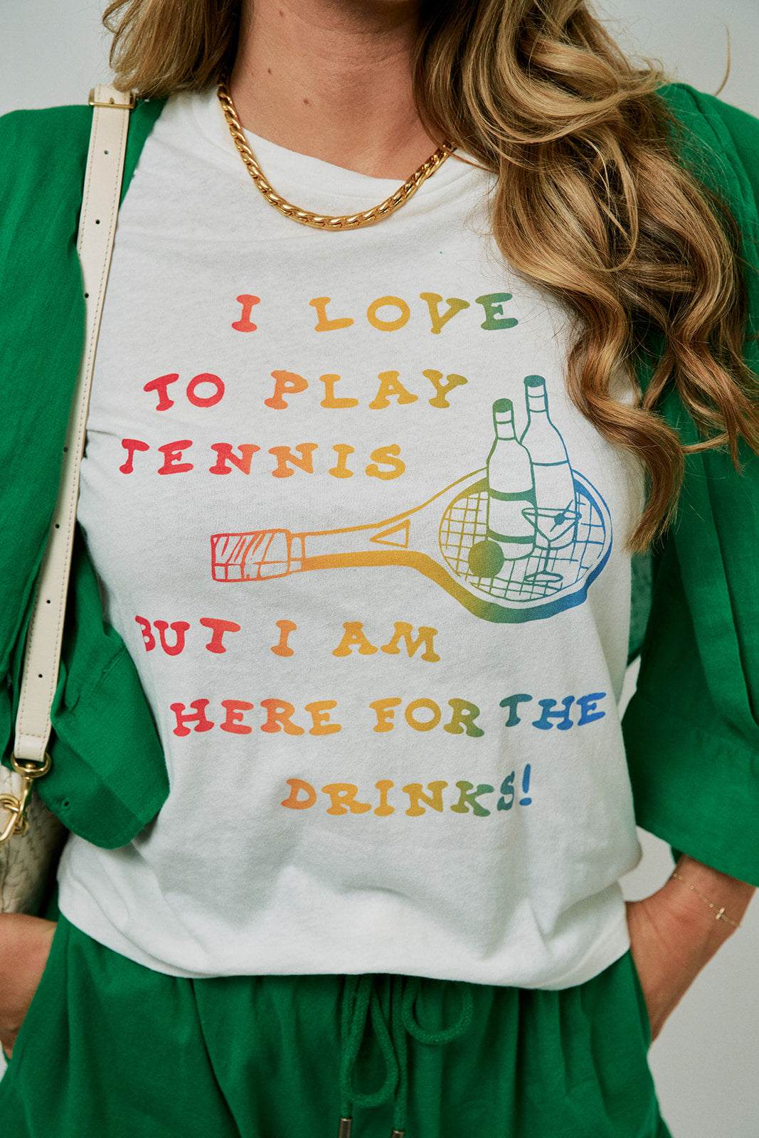 Person wearing a white t-shirt with colorful text and graphics, standing against a neutral background with Mercer Necklace