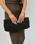 Person wearing a black and brown striped dress holding a black clutch against a plain background