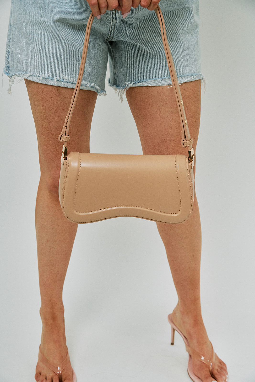 Beige handbag held by a person wearing denim shorts on a white background