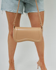 Beige handbag held by a person wearing denim shorts on a white background