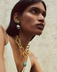Woman wearing gold chain earrings with a textured beige background
