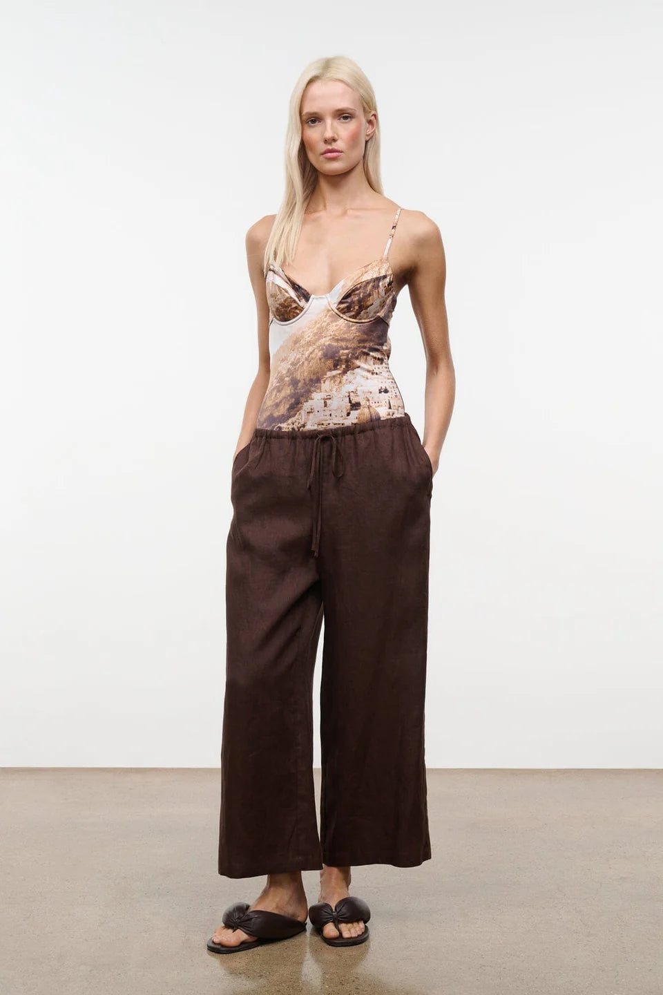 Woman wearing a patterned top and brown wide-leg pants against a white background