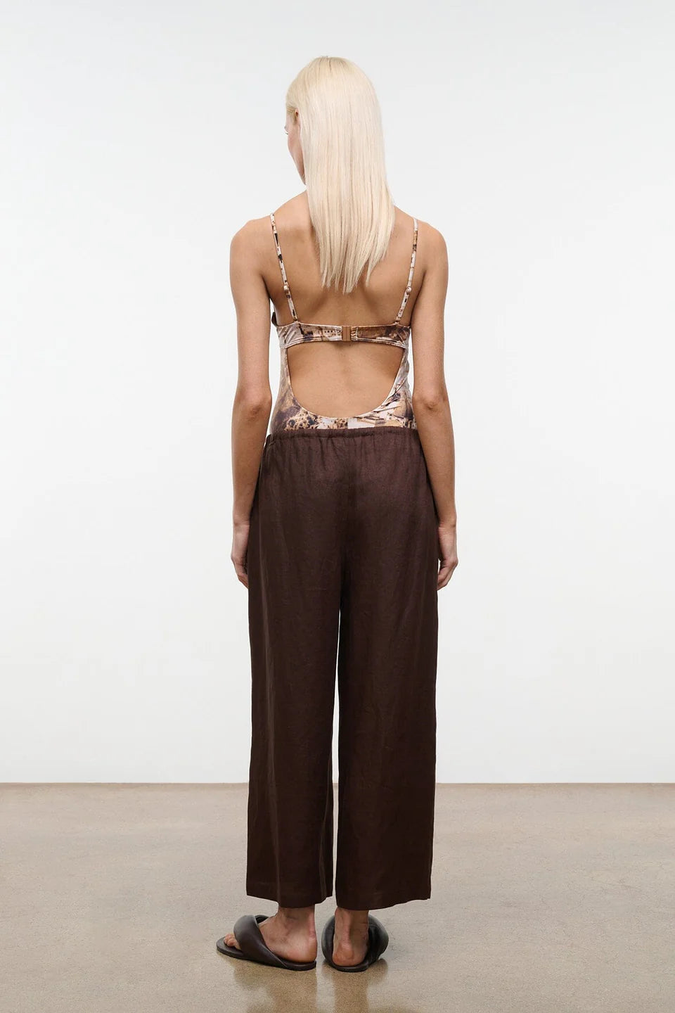 Person wearing a patterned top and brown wide-leg pants against a white background