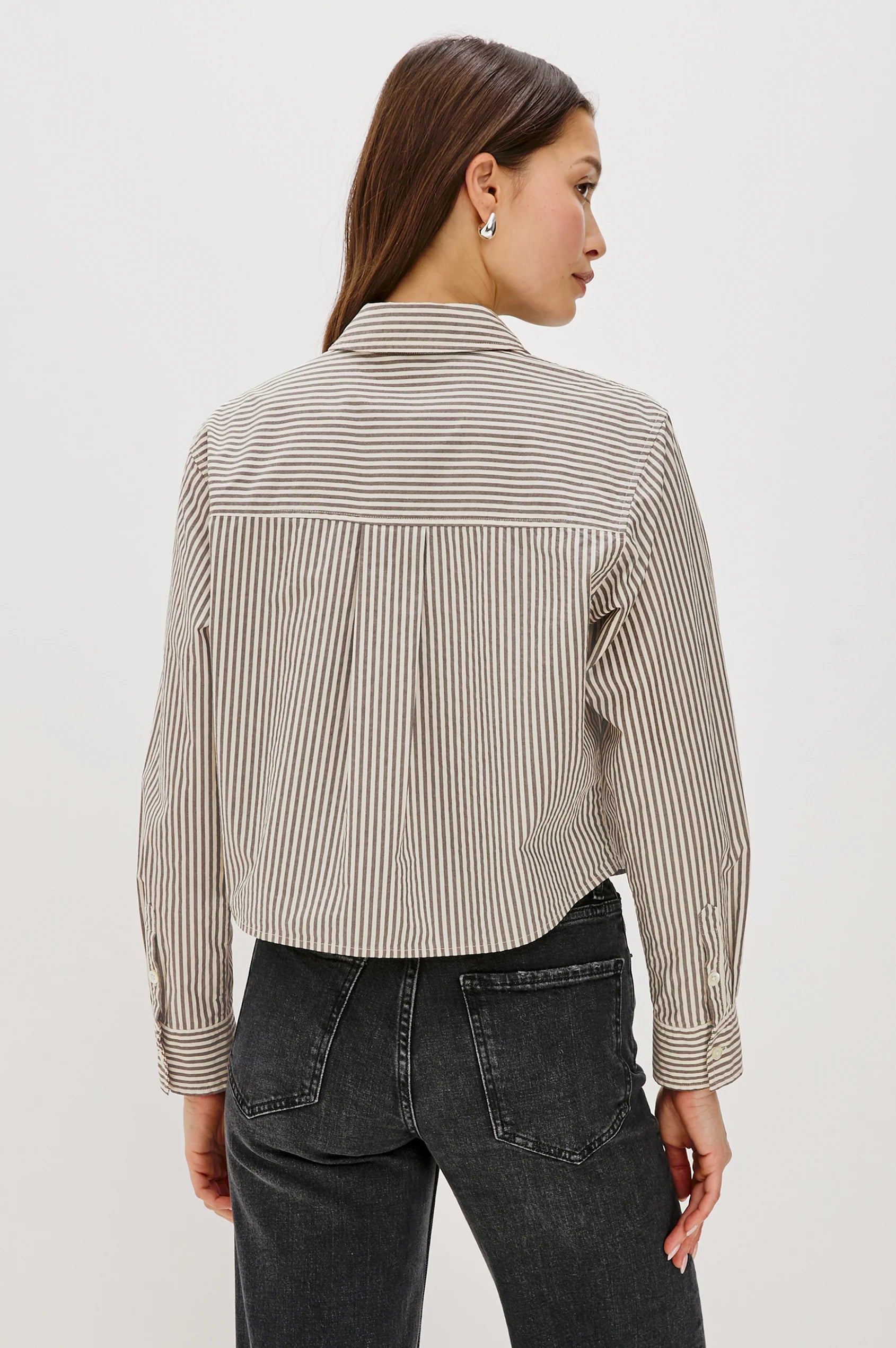 Person wearing a striped shirt and dark jeans on a white background back view