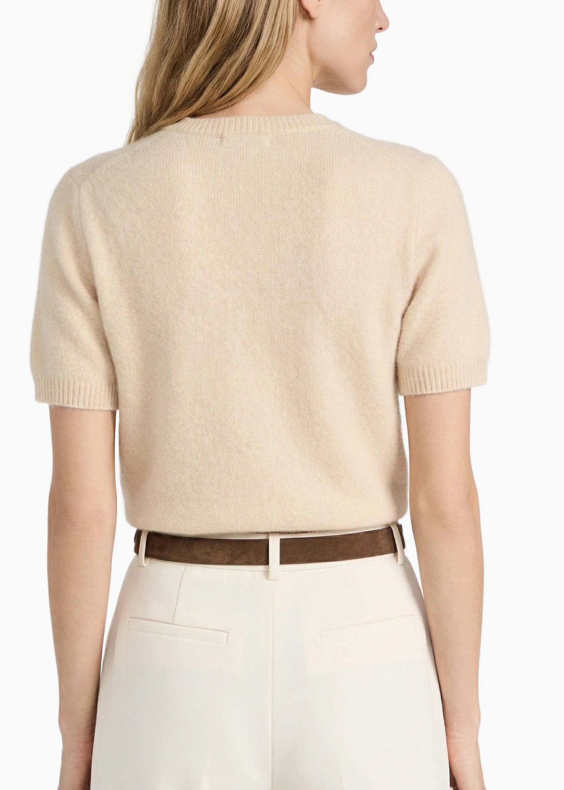 Woman wearing a beige sweater and white pants with a brown belt on a white background