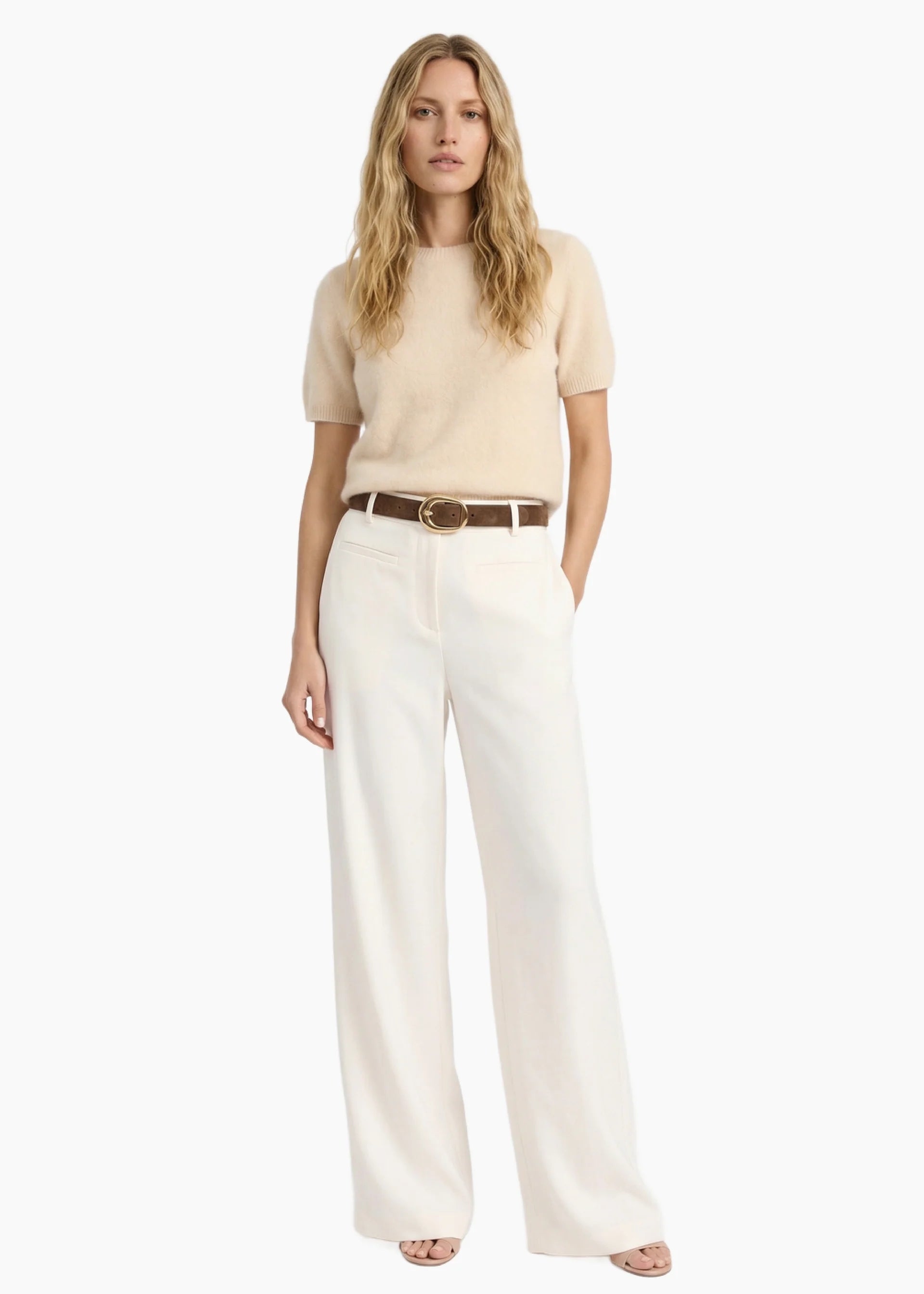 Woman wearing a beige top and white pants with a belt on a white background