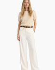 Woman wearing a beige top and white pants with a belt on a white background