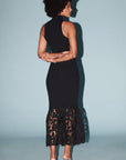 model wearing a sleeveless black dress with a lace bottom on a light blue background, back view 