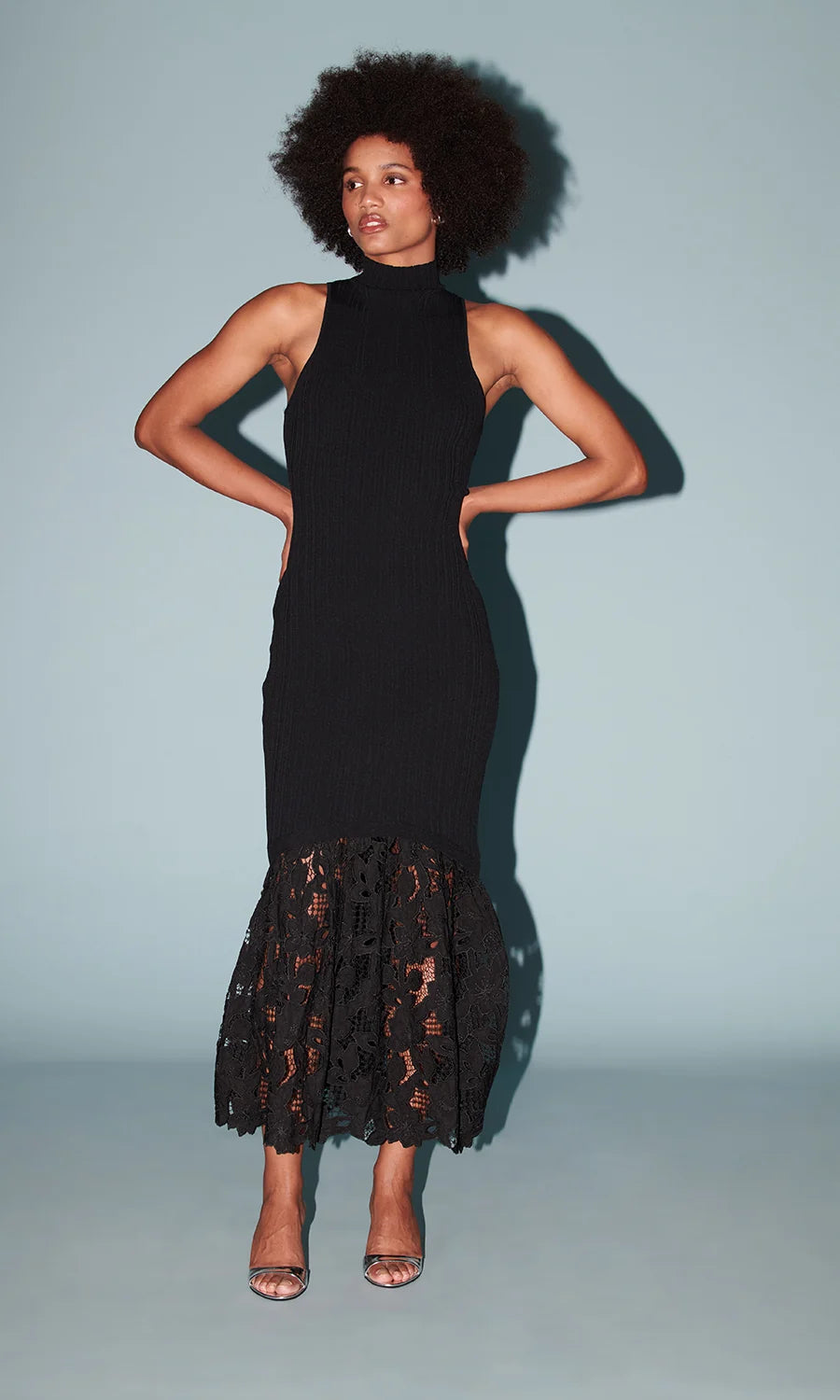 model wearing a sleeveless black dress with a lace bottom on a light blue background 