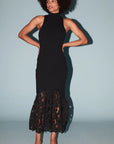 model wearing a sleeveless black dress with a lace bottom on a light blue background 