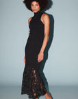 model wearing a sleeveless black dress with a lace bottom on a light blue background 