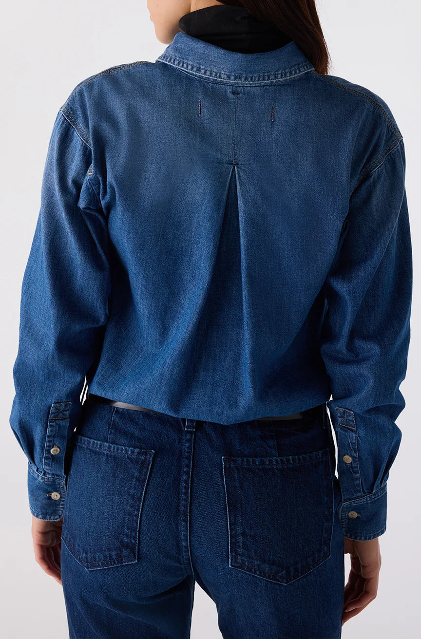 A person shown from the back wearing a dark blue denim long-sleeve button-up shirt and matching dark blue denim jeans against a plain light gray studio background.