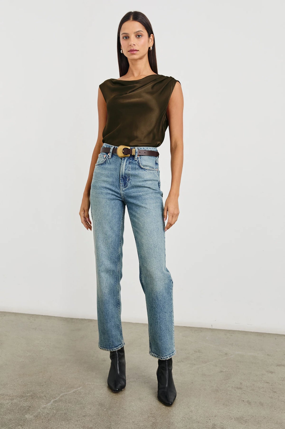 Woman wearing a green satin top and blue jeans against a white background