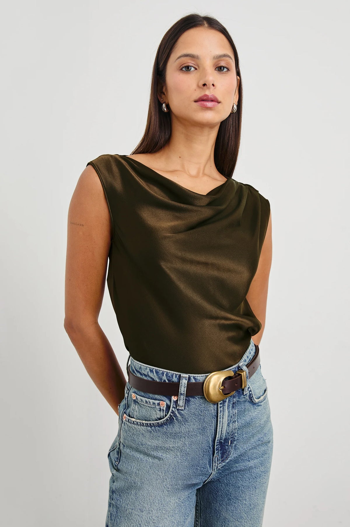 Woman wearing a brown satin top and blue jeans on a plain background