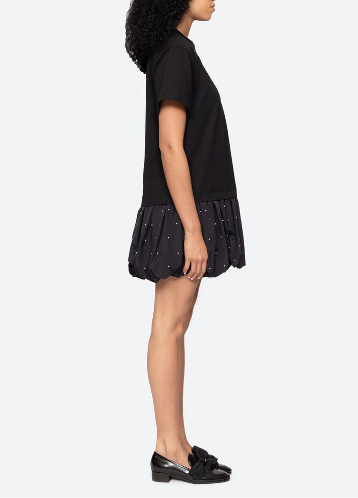 Woman wearing a black dress with ruffled bottom half on a white background