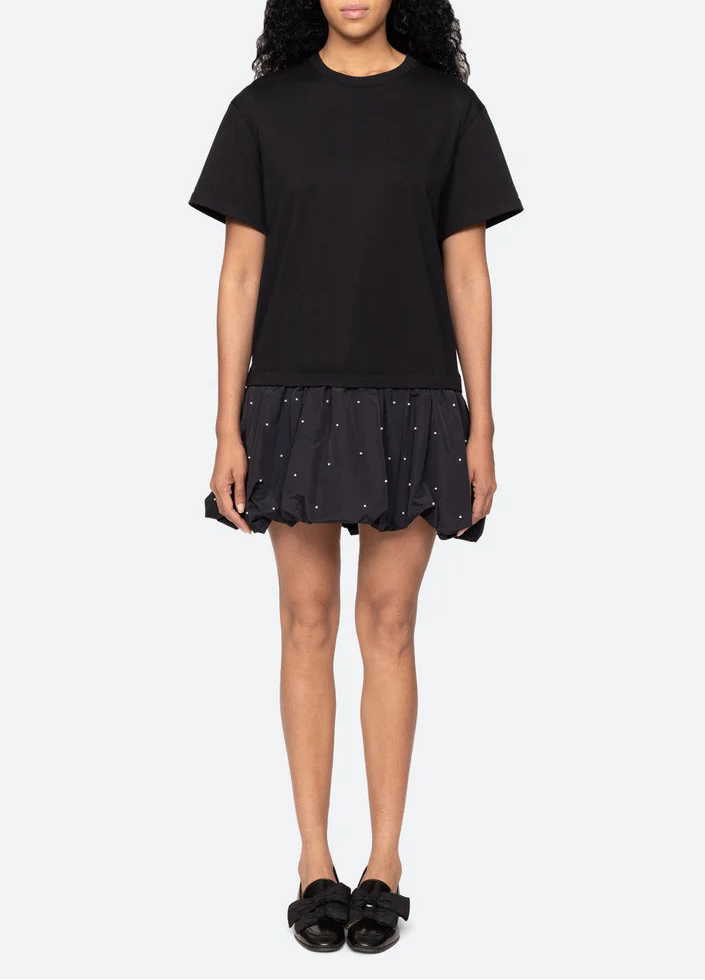 Person wearing a black t-shirt and black skirt with white polka dots on a white background