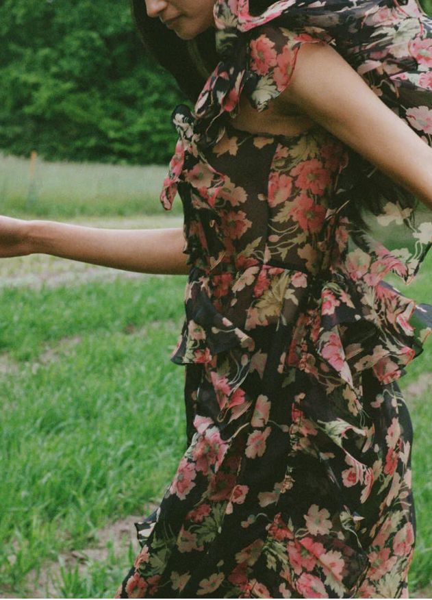 Woman in a floral dress standing outdoors with greenery in the background