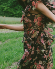 Woman in a floral dress standing outdoors with greenery in the background