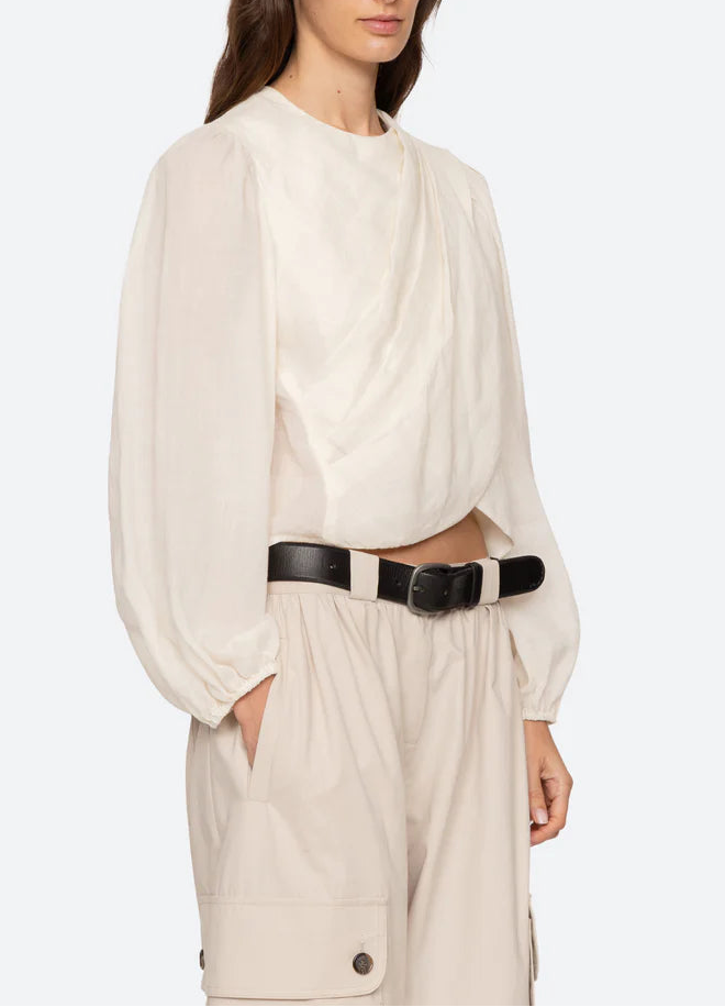 Woman wearing a white blouse and beige pants with a black belt on a white background