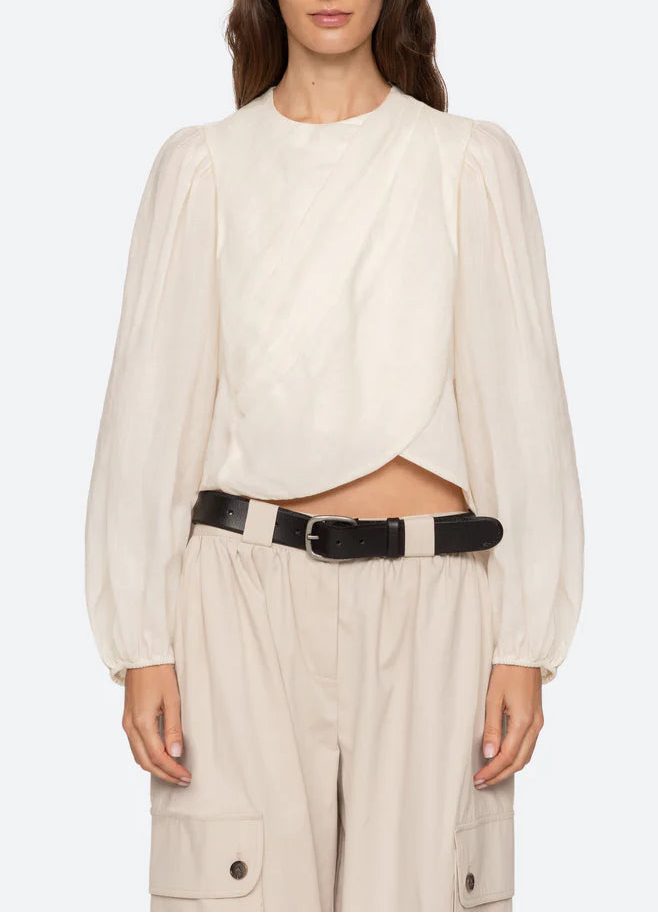 Woman wearing a white blouse and beige pants with a black belt on a white background