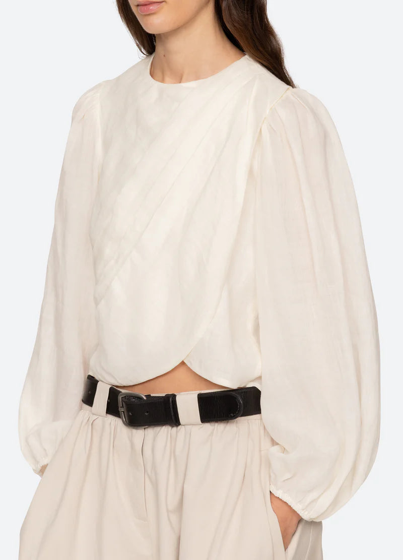 Woman wearing a white blouse with a black belt against a white background