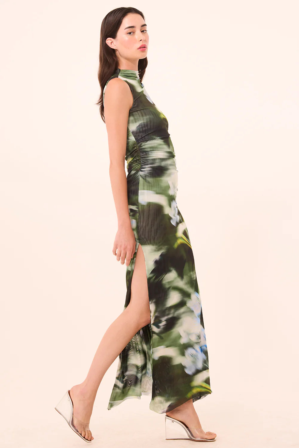 Woman wearing a green floral dress with a slit on a beige background