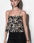 Woman wearing a black and gold patterned top with black shorts on a white background