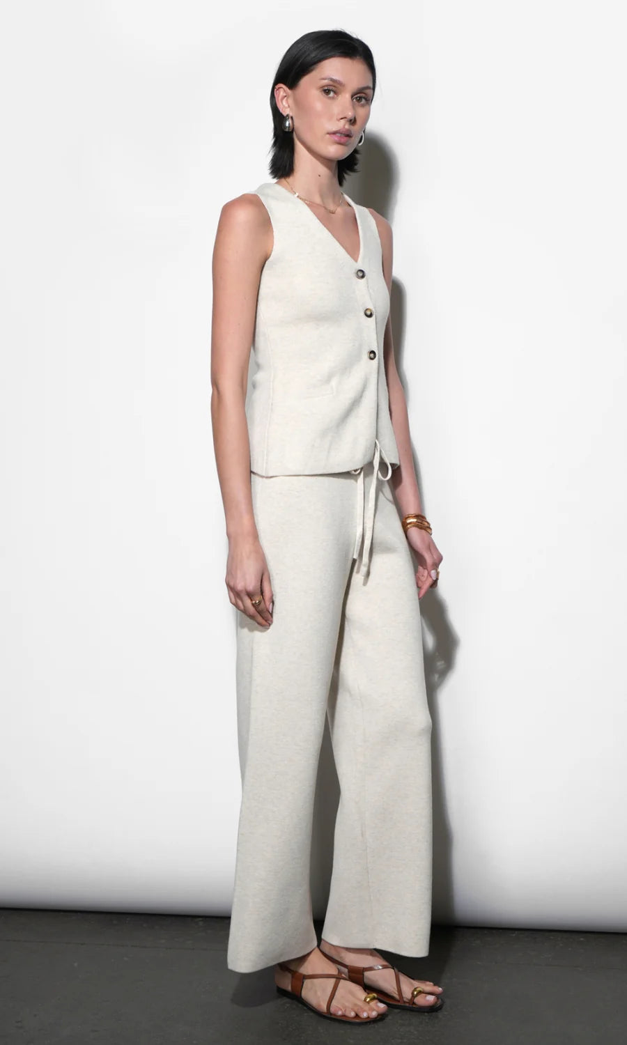 Woman wearing a white sleeveless top and wide-leg pants against a plain background